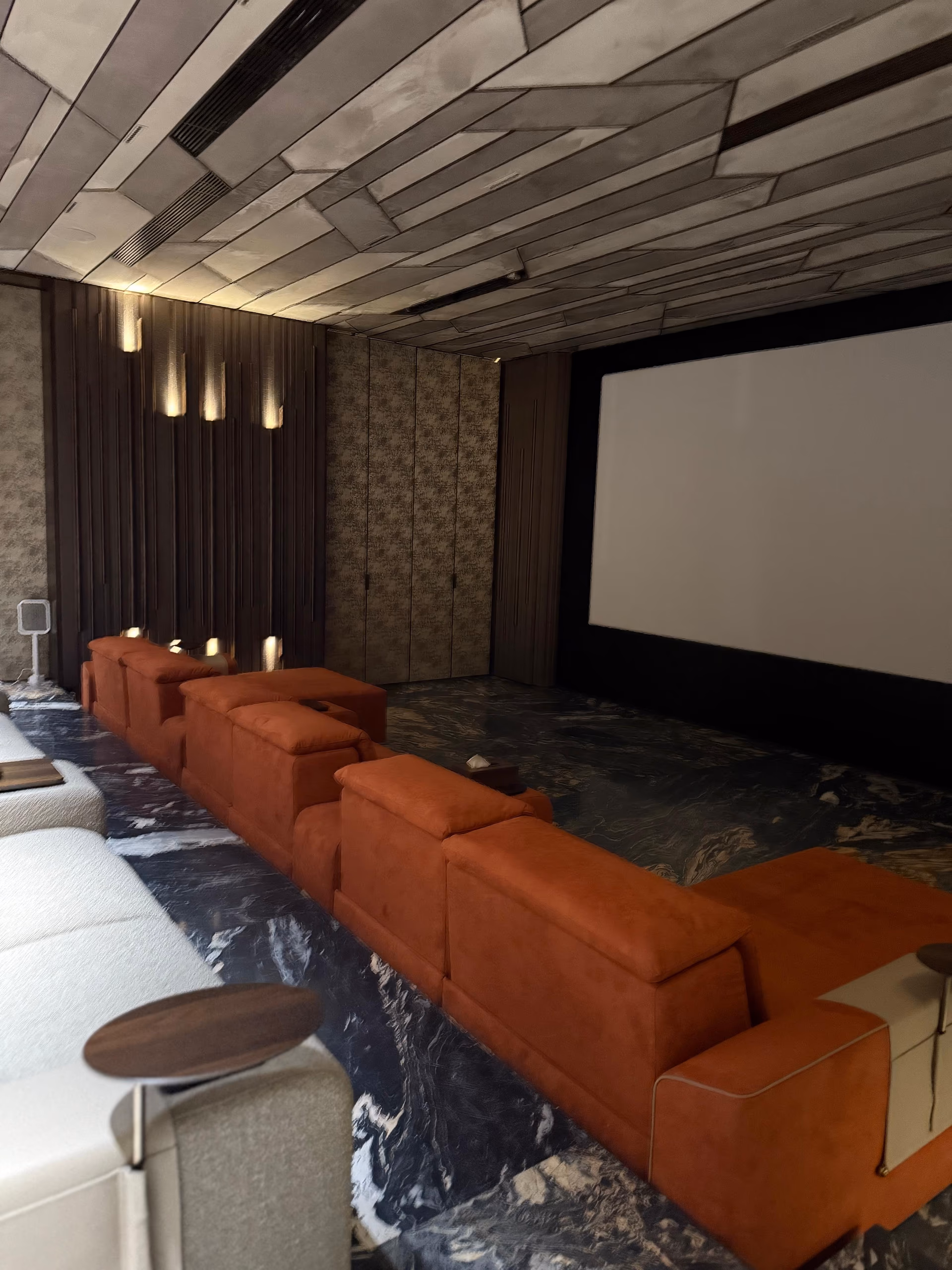 Home theater with a burnt-orange modular recliner sofa facing a large projector screen, set on a dark marble floor.
