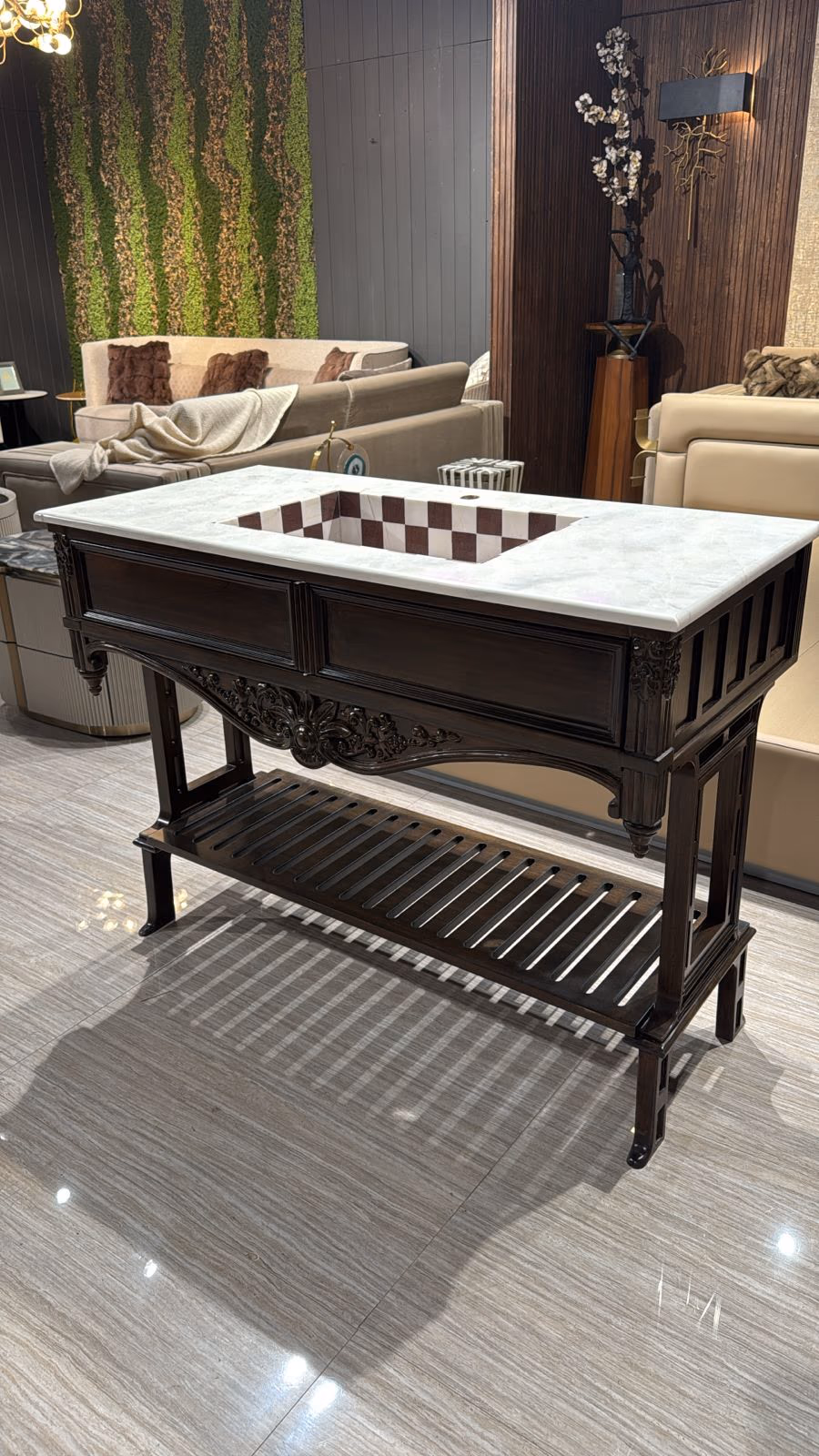 Dark carved-wood bathroom vanity with a white marble top, checkerboard-tiled inset basin and a slatted lower shelf