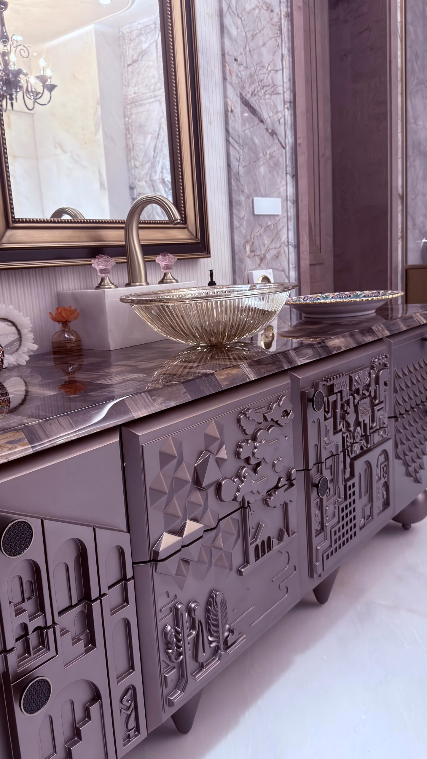 Close view of the relief vanity's ribbed champagne glass vessel bowl and brushed tap on the agate stone top, with the sculpted pewter doors below.