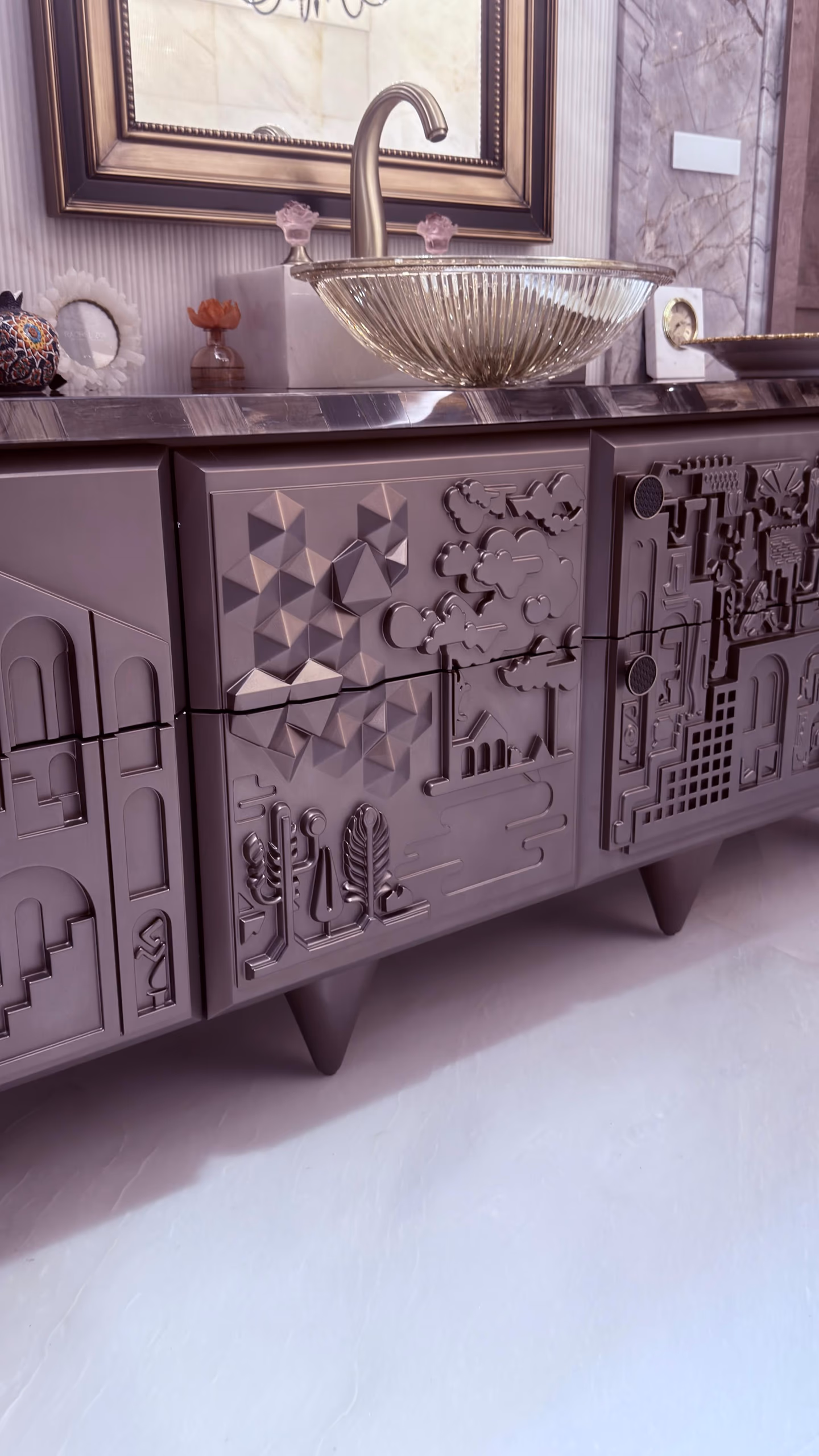 Close angled view of the pewter relief vanity's doors, showing sculpted clouds, arches, pyramids and tiny buildings under an agate top and champagne glass bowl.