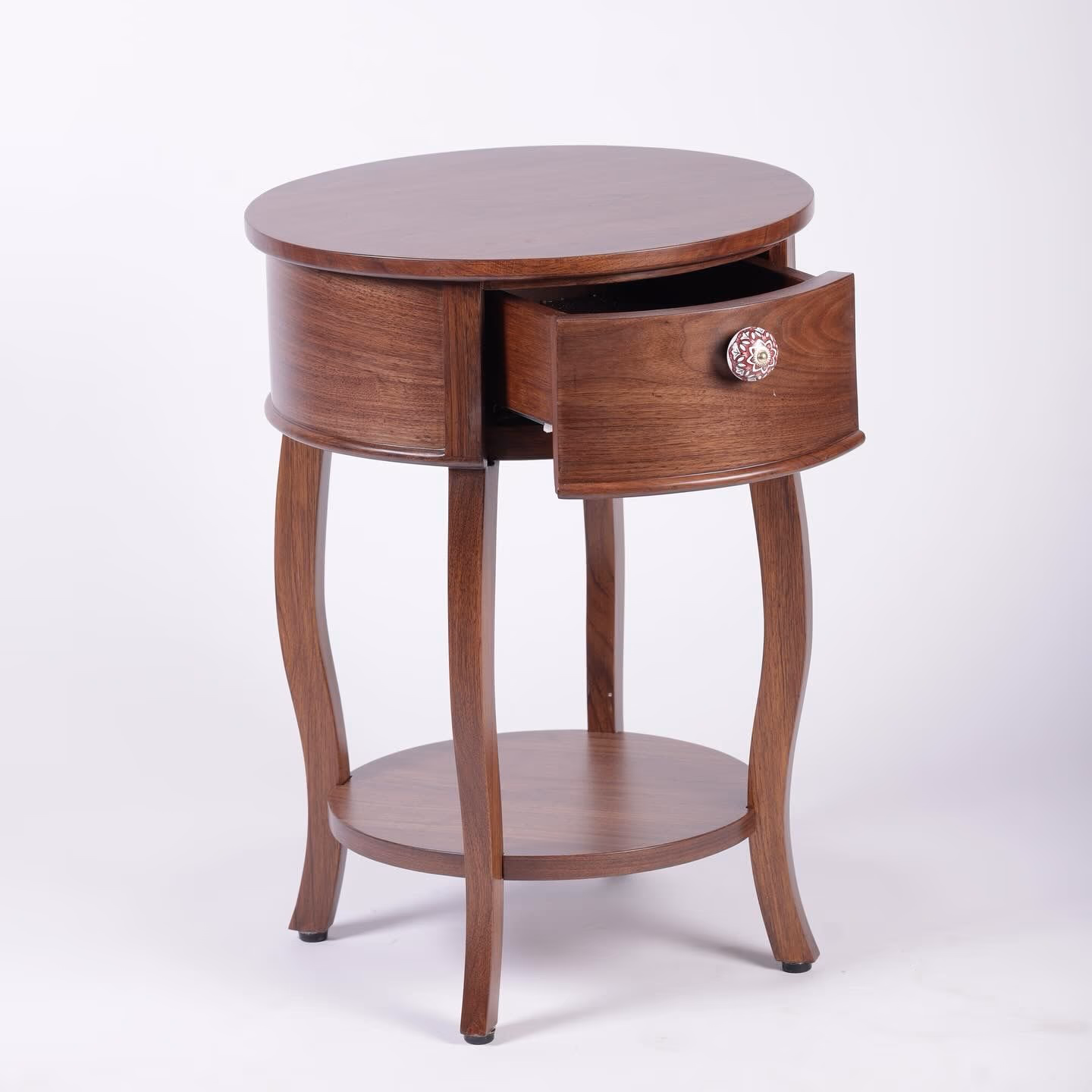 Round wooden side table with curved cabriole legs, one open drawer with a floral ceramic knob, and a lower shelf.