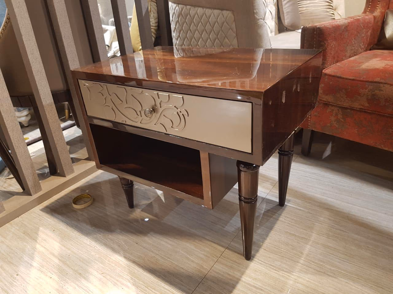Glossy walnut bedside table with one grey lacquer drawer carved with a foliate scroll and brass knob, an open shelf below and turned dark legs.