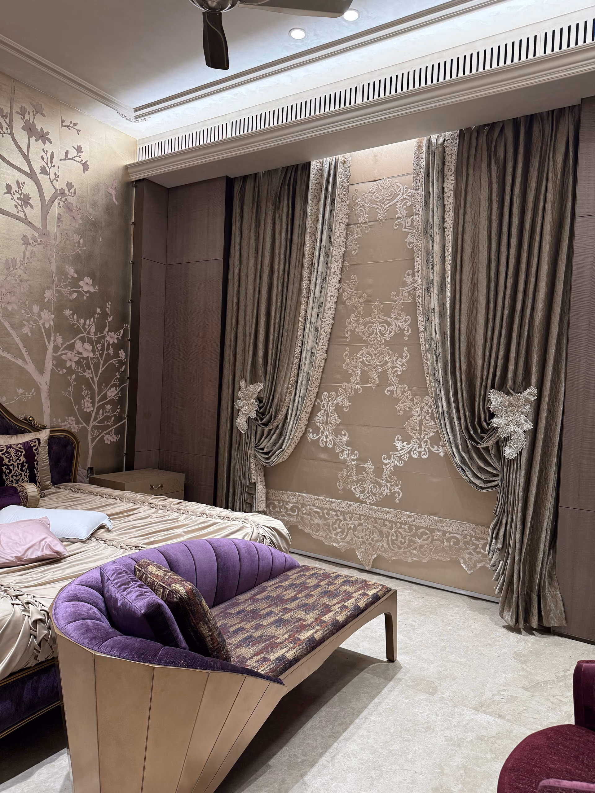 Purple channel-tufted velvet bench with a patterned seat cushion, placed at the foot of a bed before an embroidered curtain wall.