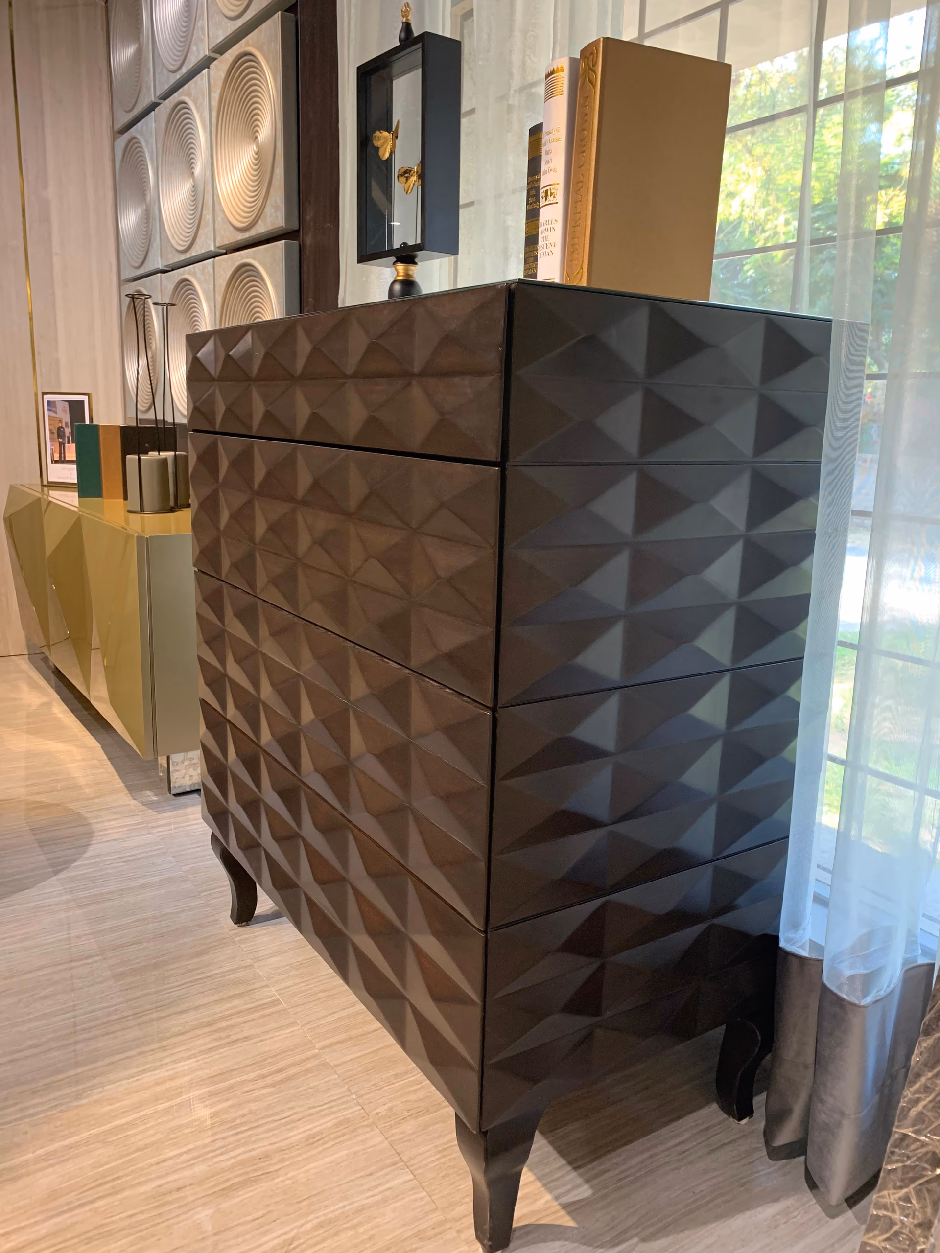 Tall dark-brown chest of drawers with a three-dimensional diamond-faceted front that catches light in triangles, standing on short curved legs.