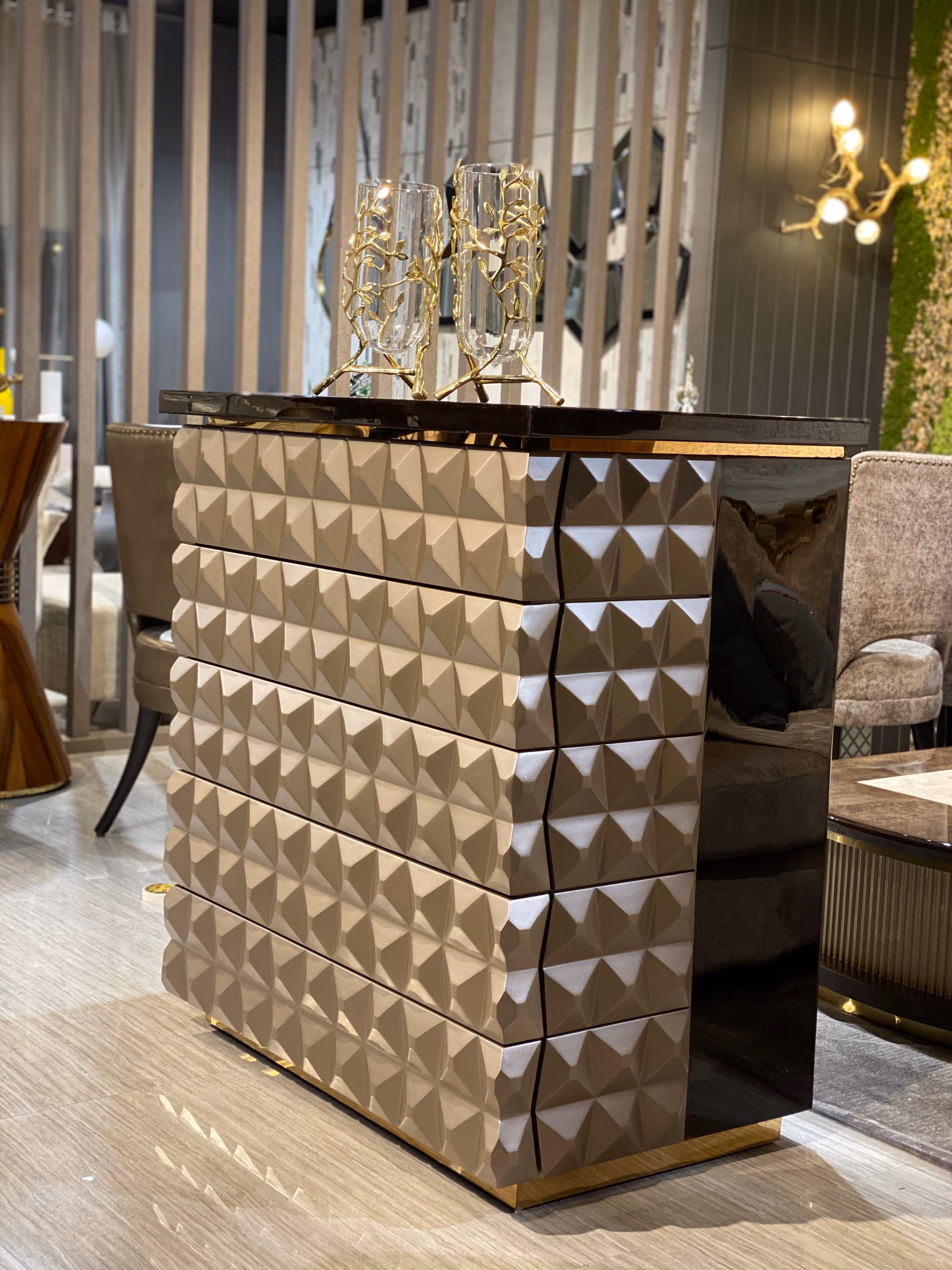 Chest of drawers with champagne drawer fronts carved into raised pyramid facets, flanked by glossy dark side panels and set on a slim brass base.