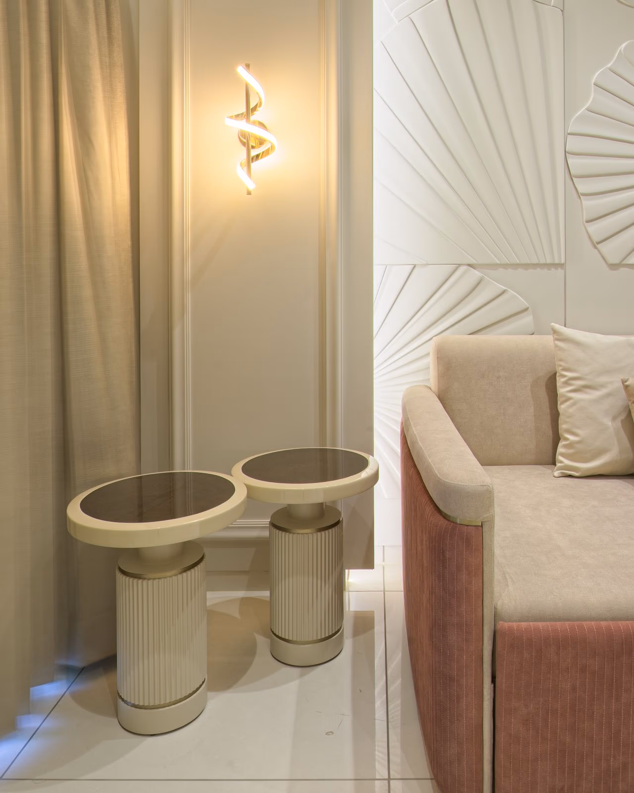 Two round cream side tables with fluted pedestal bases and black marble-effect tops beside a blush sofa bed.