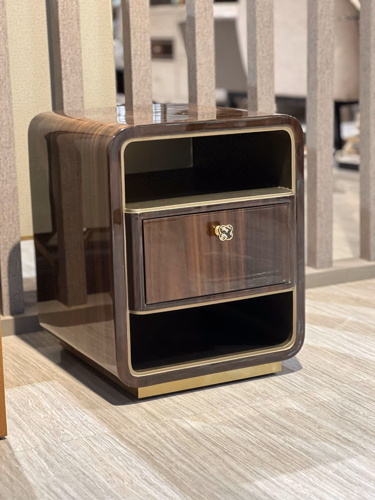 Glossy dark wood nightstand with an open top shelf, one drawer with a clover-shaped brass pull, and an open lower shelf.