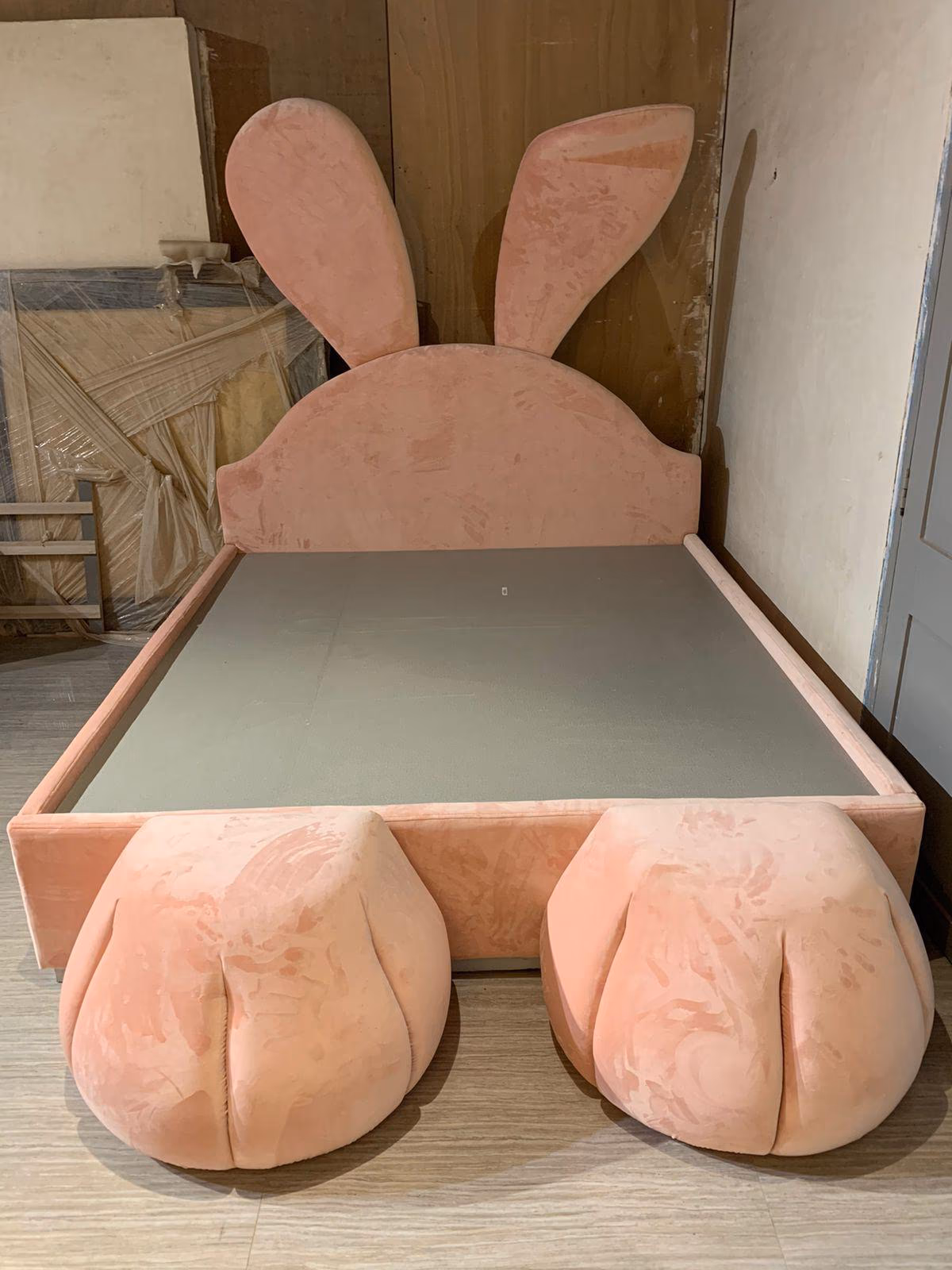 Blush pink velvet upholstered children's bed with tall bunny-ear headboard and two round padded bunny-paw shapes at the foot.