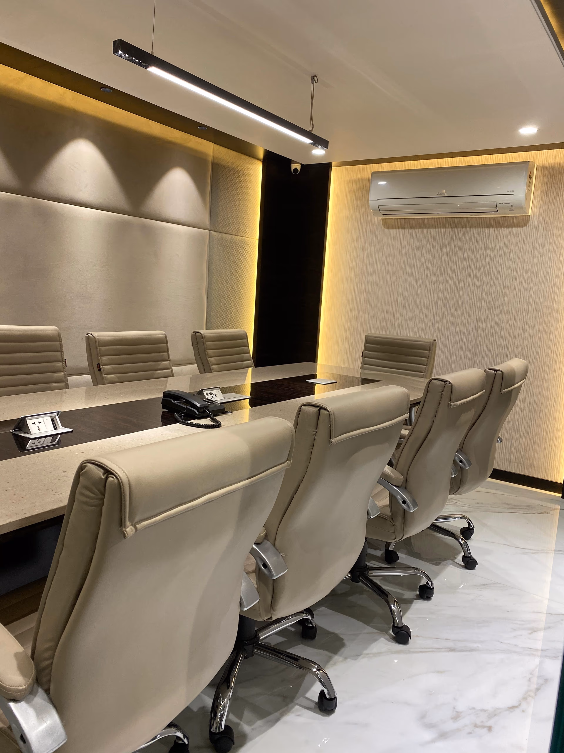 Long boardroom conference table with a dark wood body and inset stone top, ringed by high-back beige leather executive chairs.