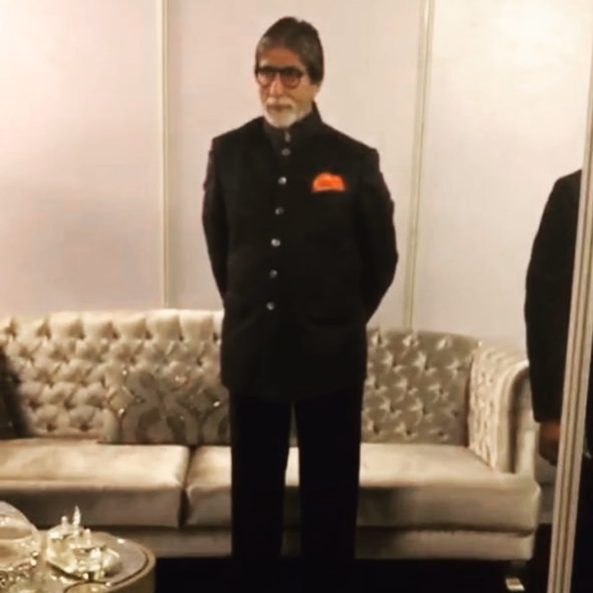 Amitabh Bachchan standing beside a silver deep-buttoned Designatore sofa and matching side tables.