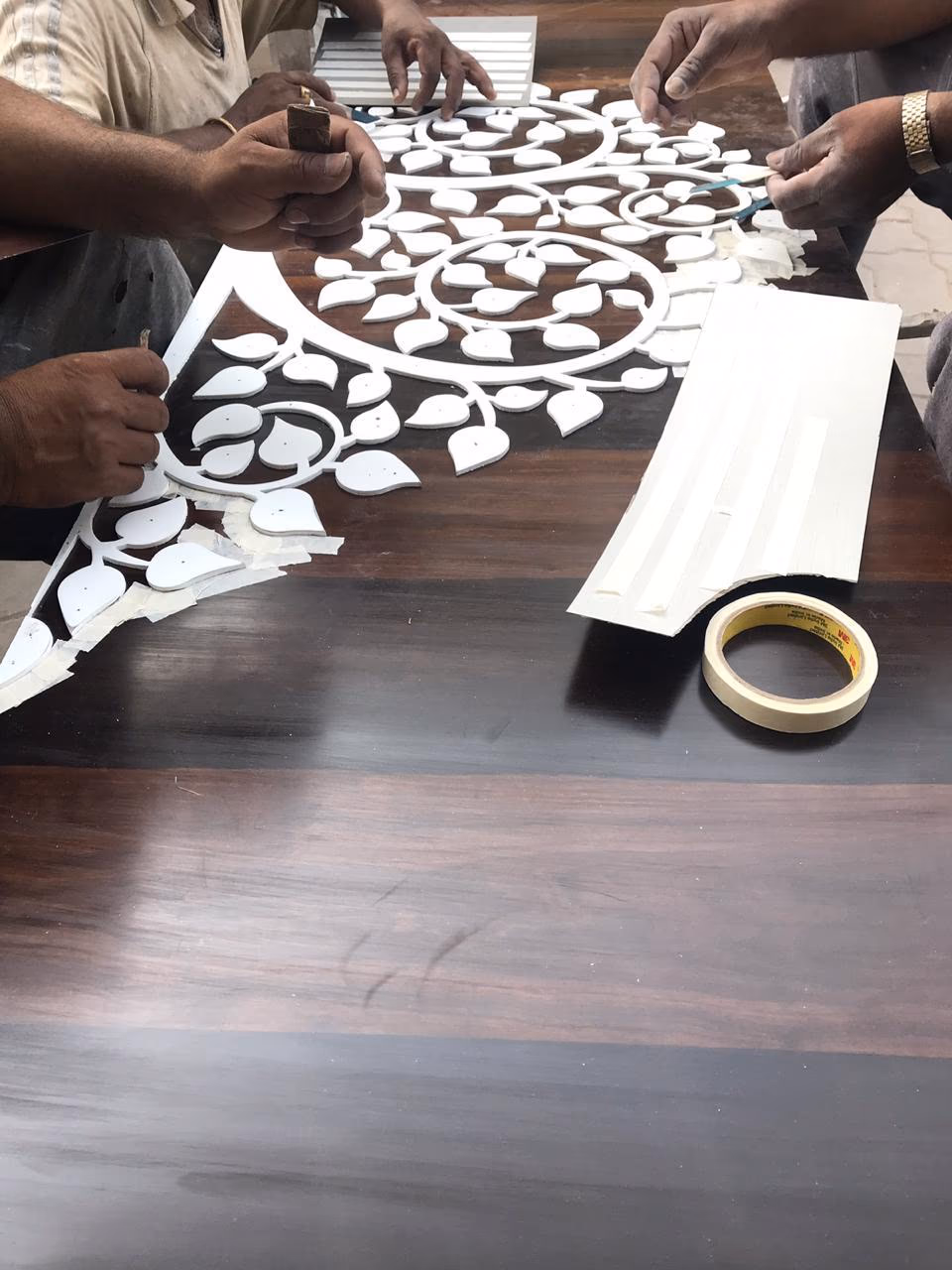 Hands laying a peepal-leaf mandala inlay into a dark wood surface.