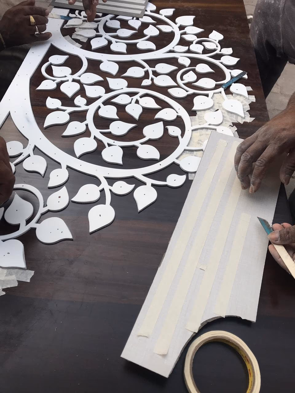 Artisans hand-cutting a tree-of-life stone inlay panel for a bespoke furniture commission in India.