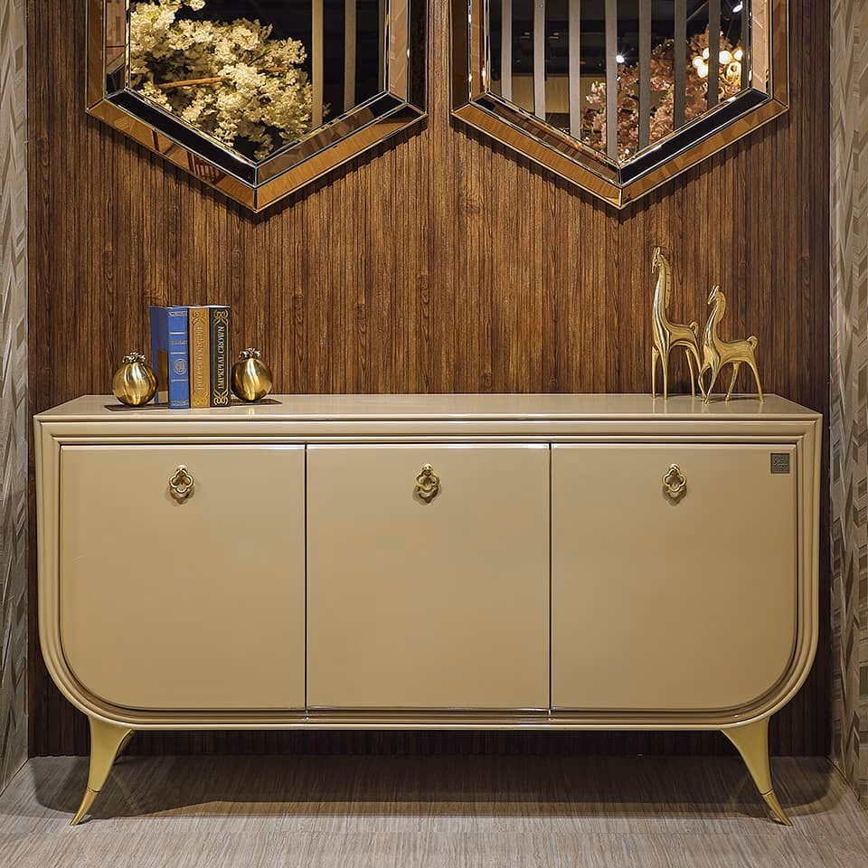 Three-door sideboard in soft beige lacquer with rounded corners, antique-brass ring pulls and splayed brass-tipped legs, shown below two bronze-glass wall mirrors.