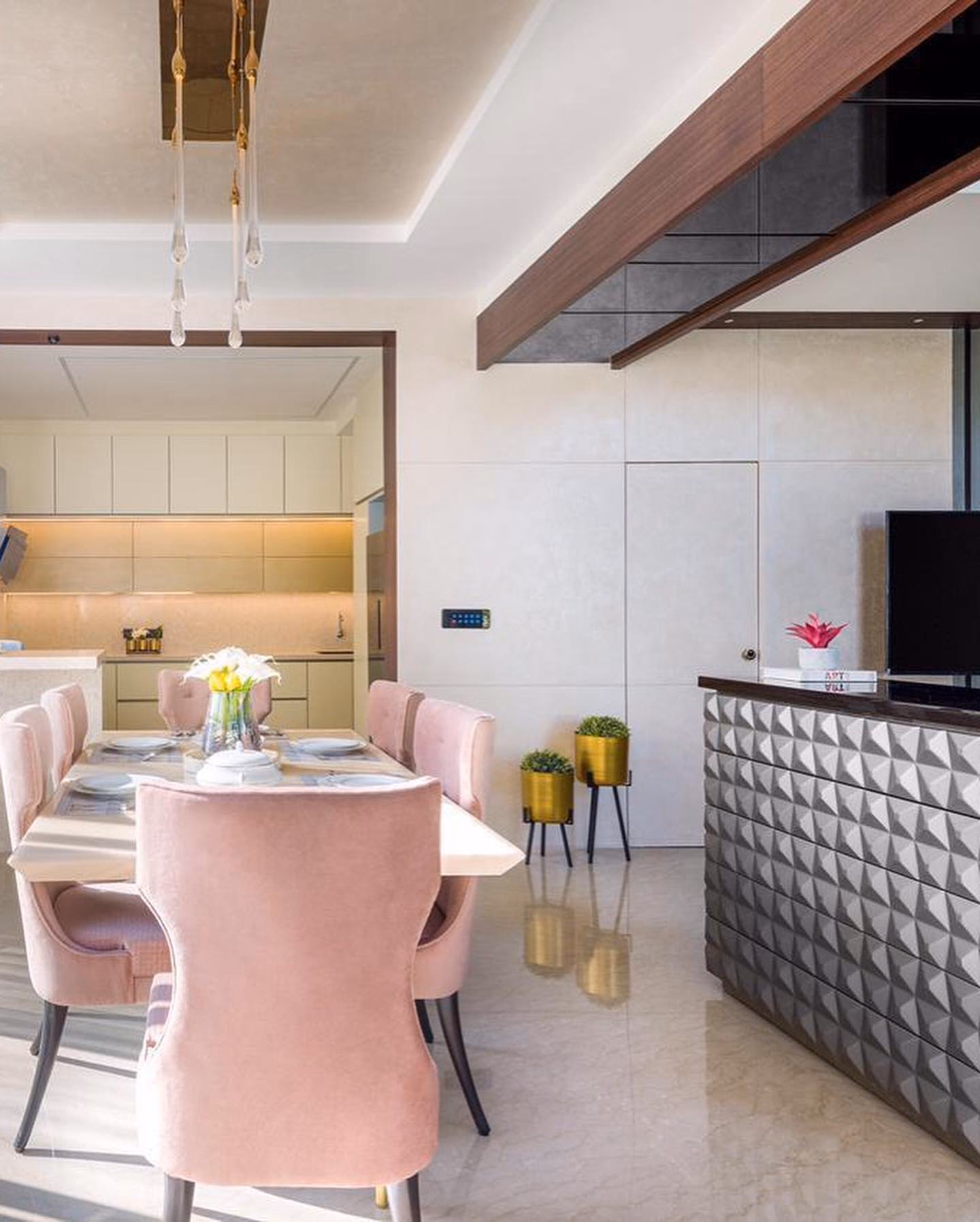 Open-plan dining set with a pale marble-top table and six blush pink velvet wingback dining chairs on dark tapered legs, beside a faceted grey stone breakfast counter.