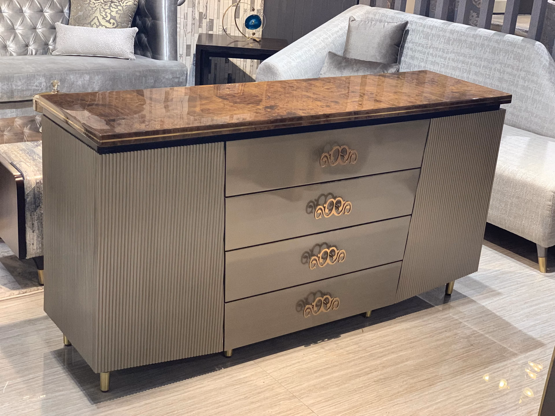 Sideboard with a glossy walnut-burl top and brass edge, fluted grey side cupboards and four central drawers with gold scroll handles, on slim brass feet.