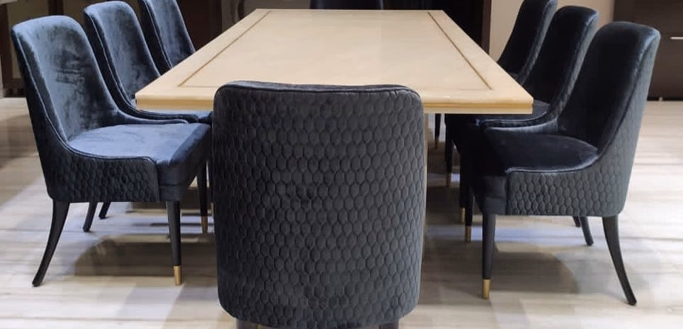 Ten-seat dining set with a cream stone top framed in a fine gold inset line, surrounded by charcoal velvet chairs with honeycomb-quilted backs and brass-capped tapered legs.