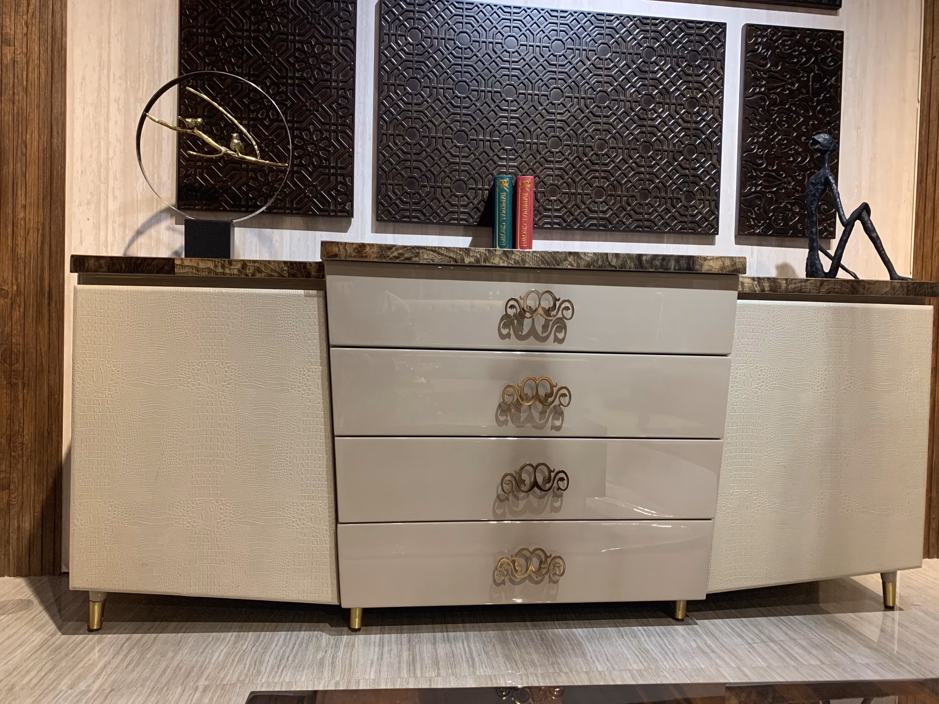 Cream sideboard with crocodile-textured end doors, four gloss centre drawers with gold baroque scroll handles and a dark figured-marble top.