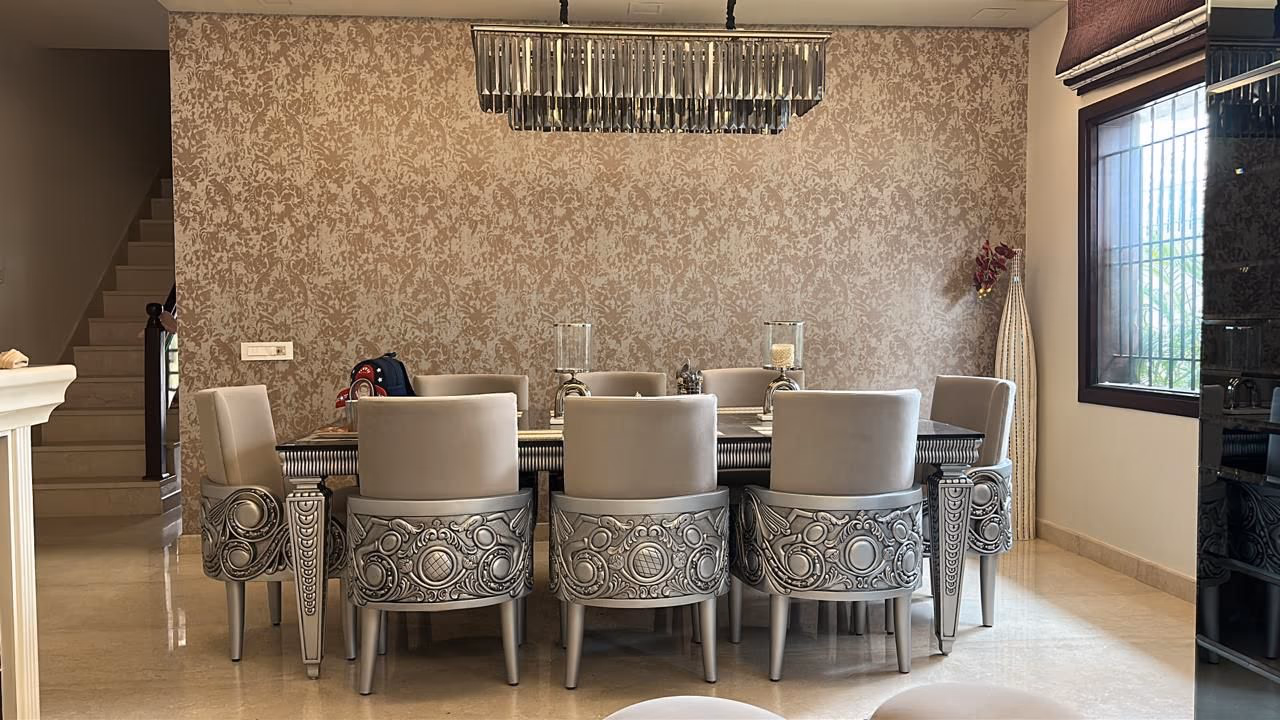 Eight silver carved-base dining chairs around a long dark table beneath a crystal chandelier in a home dining room.
