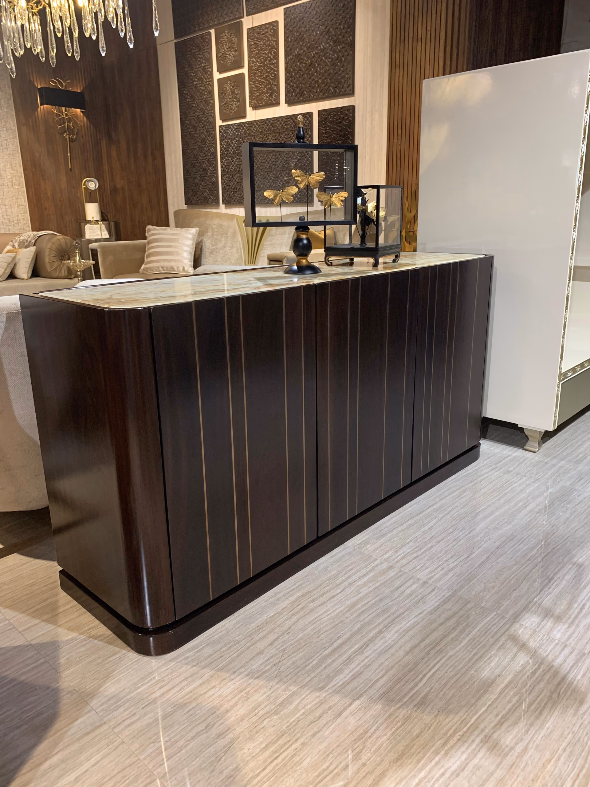Dark ebony sideboard with fluted doors lined by thin brass inlay and a pale green-and-gold onyx top, standing on a curved wood floor.
