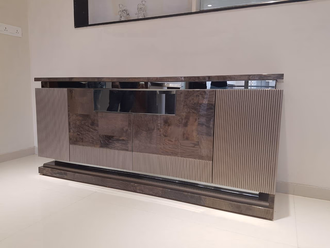 Low sideboard with high-gloss burl wood centre doors, fluted taupe side panels, a dark glossy top and a floating stepped plinth base.