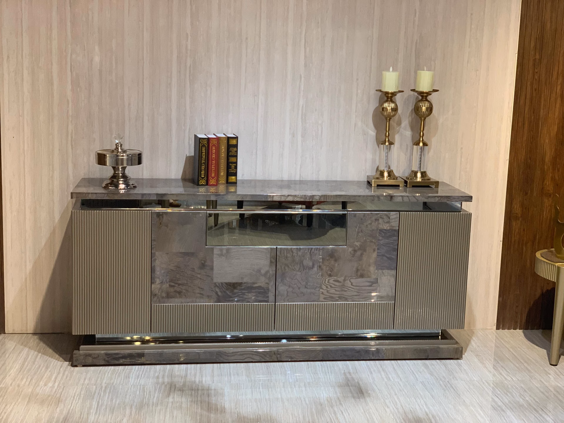 Slightly angled view of the same fluted grey sideboard, showing its full length, stone top edge and reflective steel base against a pale wall.
