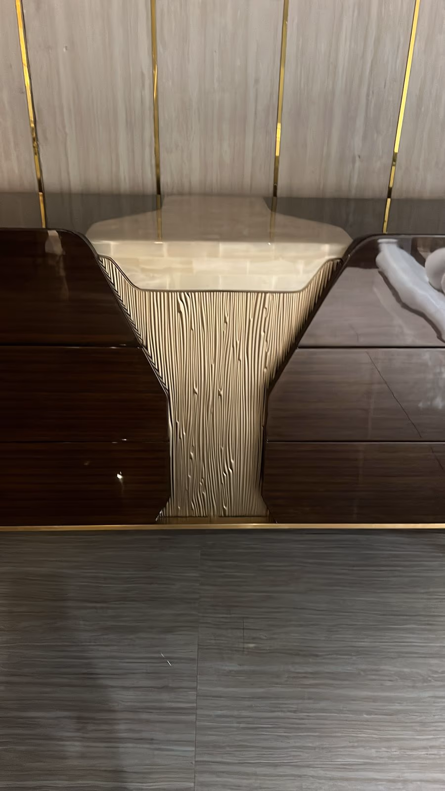 Close-up of a cream fluted trumpet-shaped table leg between two dark glossy tabletop surfaces with brass trim.