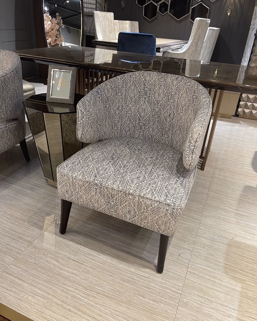 Low barrel-back accent chair upholstered in a grey and cream diamond jacquard weave, with a curved wrap-around back and dark tapered wooden legs.