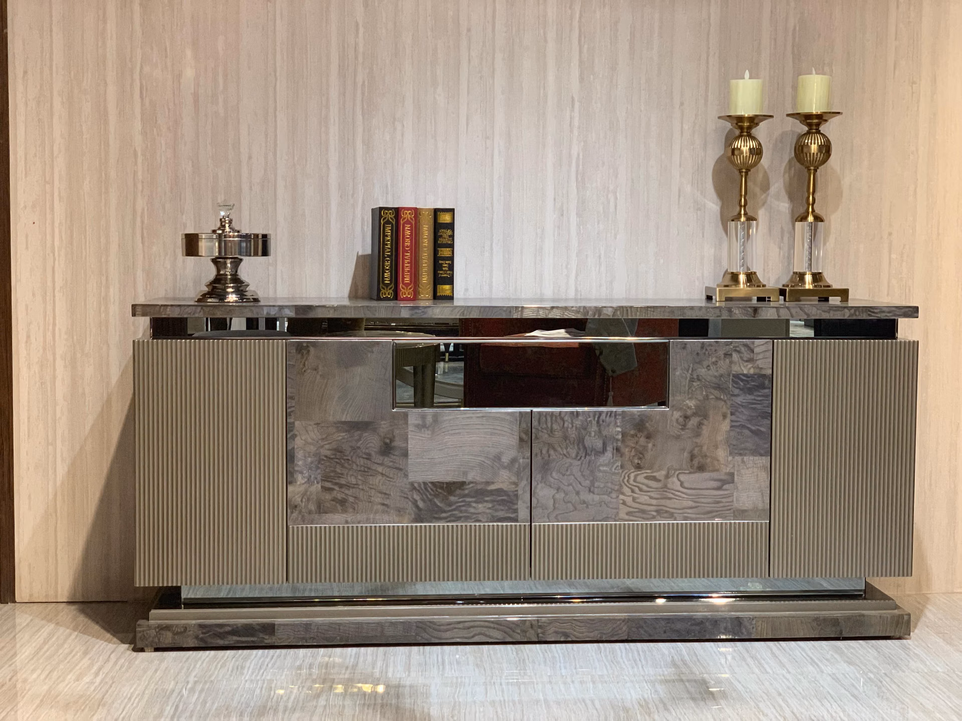 Low sideboard with fluted light-grey sides, mirror-polished burl centre doors, a thick grey stone top and a bright steel plinth, styled with candles and books.