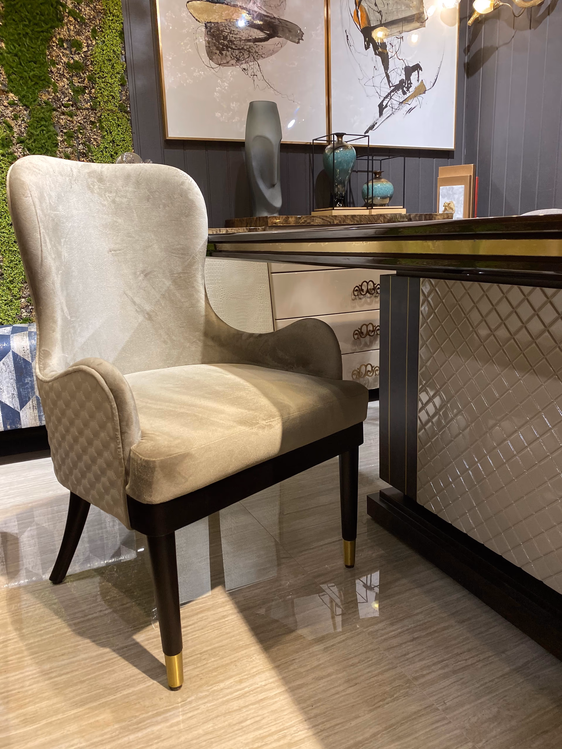 High-back wingback dining chair upholstered in cream honeycomb-quilted fabric with curved arms, standing on dark wood legs tipped with brass caps.