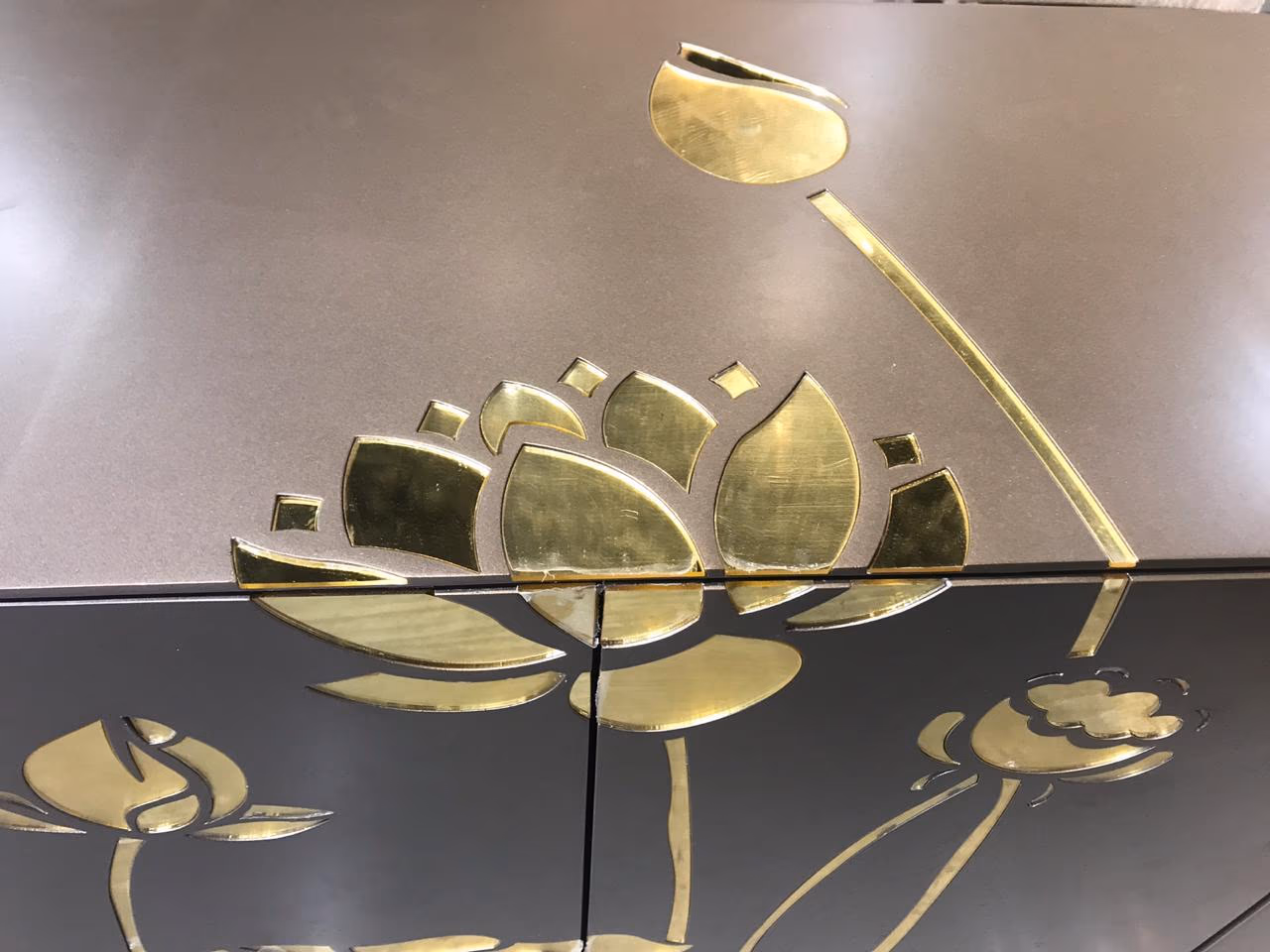 Close-up of the brass lotus inlay on a bronze-grey sideboard, showing the fine hand-cut petals and stems laid flush into the matte cabinet surface.