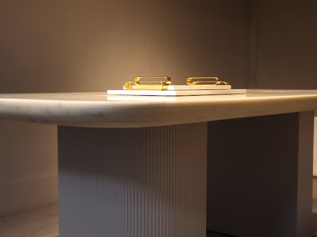 Close-up of a white-grey marble table edge and fluted pedestal leg with two amber glass tumblers on a white tray.