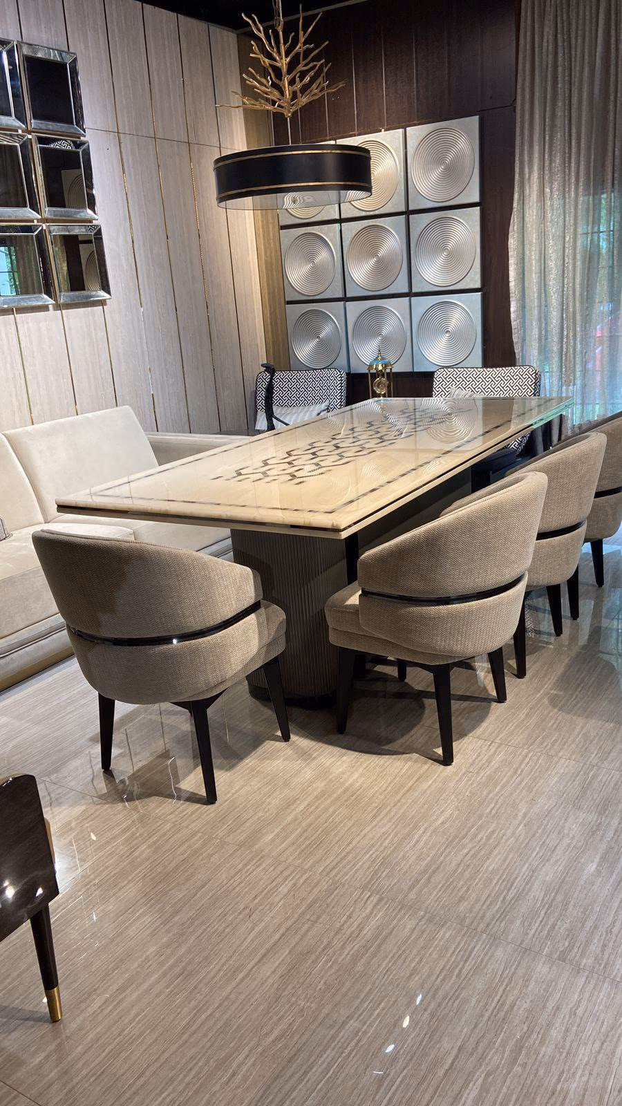Dining room with a marble-pattern table on a dark fluted pedestal, six barrel-back chairs and a branch pendant light.