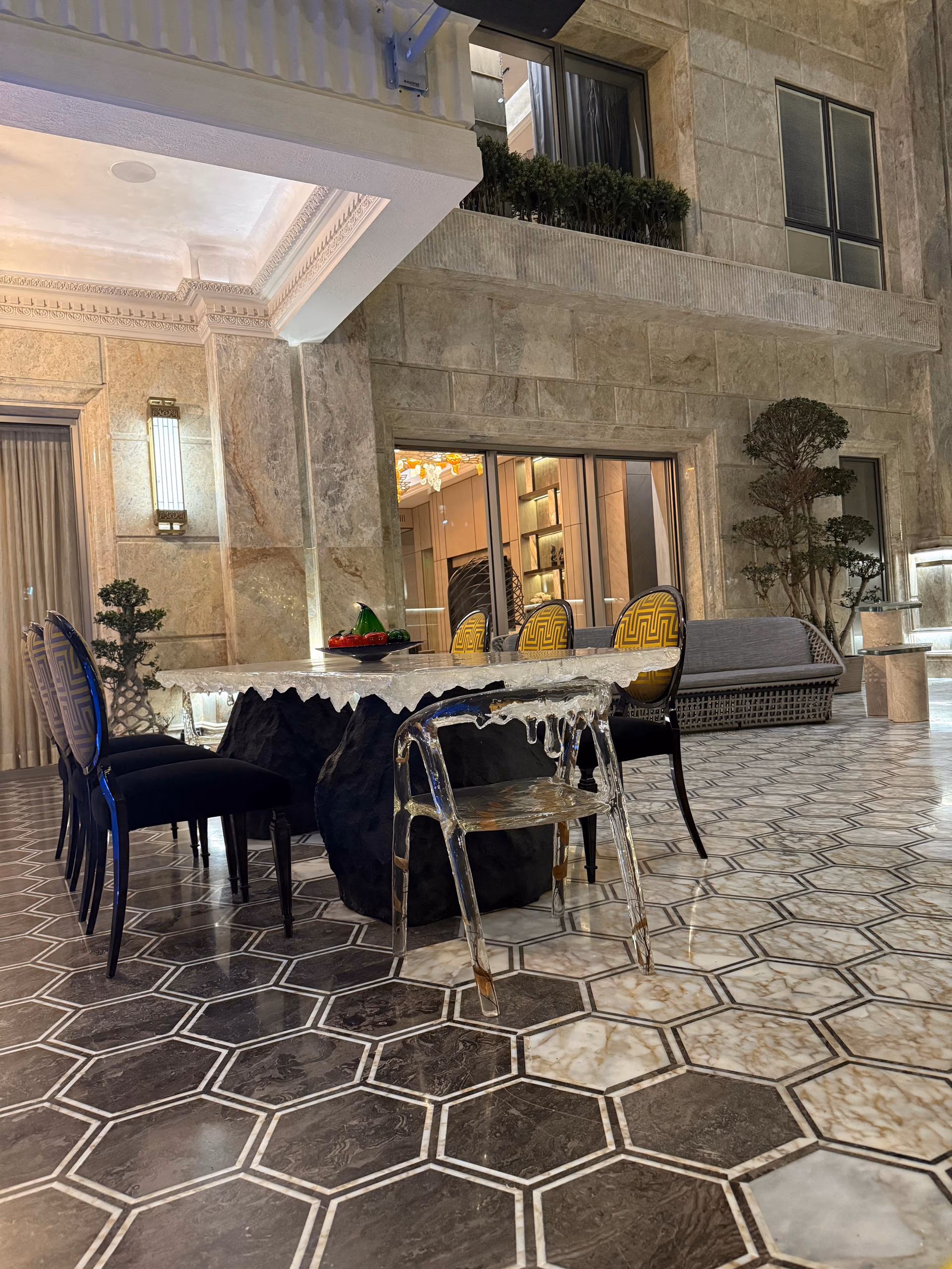 Dining table with a dripping ice-white resin top over a black rock-form base, surrounded by mixed dark and clear acrylic chairs.