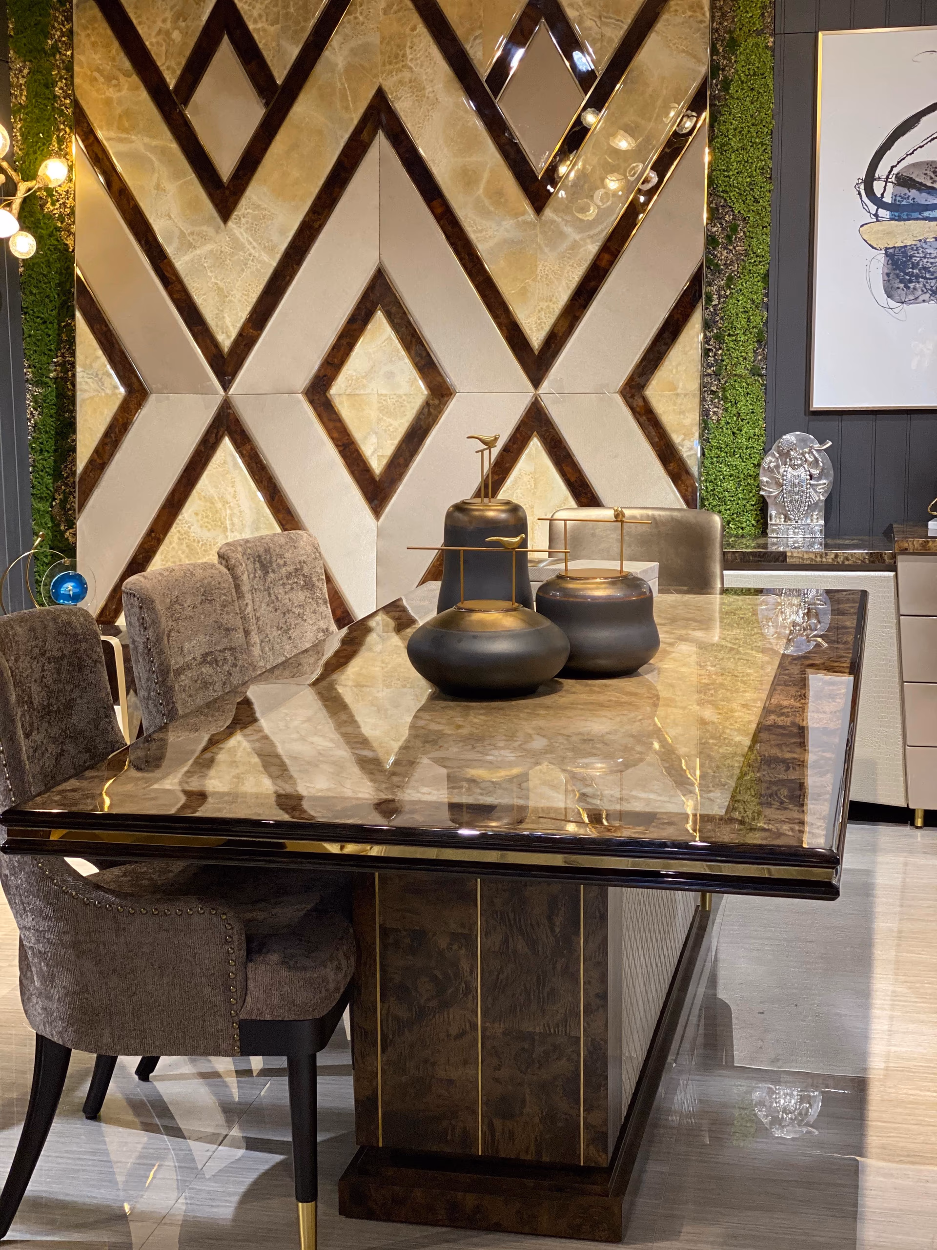 Glossy onyx burl pedestal dining table with upholstered chairs against a chevron feature wall