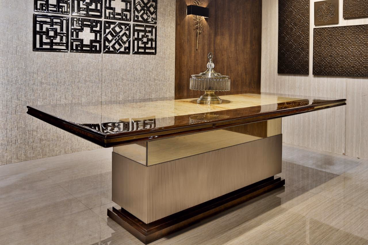 Three-quarter view of the burl-and-onyx dining table showing the fluted champagne pedestal and stepped dark plinth on a polished stone floor.