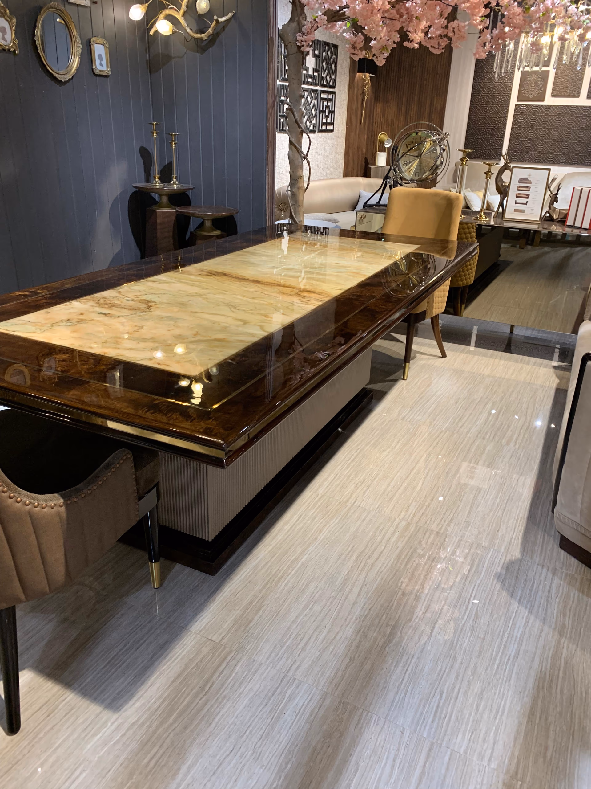 The burl-and-onyx dining table seen from the end with tan velvet dining chairs tucked along one side in a warm showroom setting.