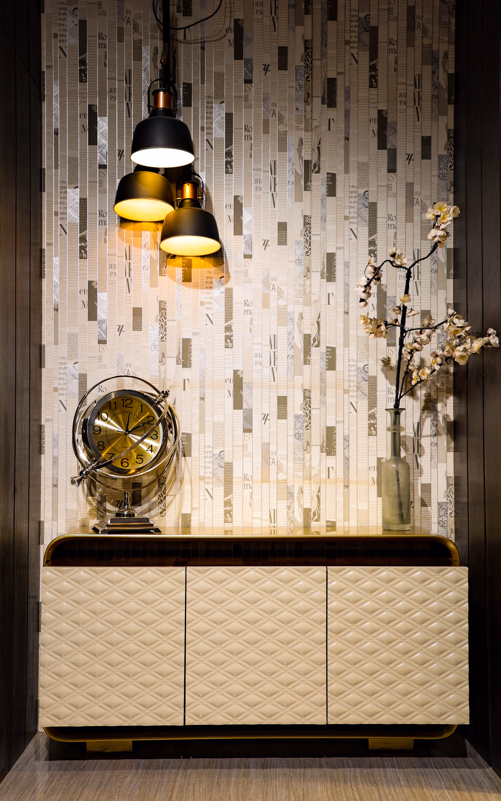 Cream quilted-front buffet with brass top trim, glass table clock and flowering branch in a lit wall niche.