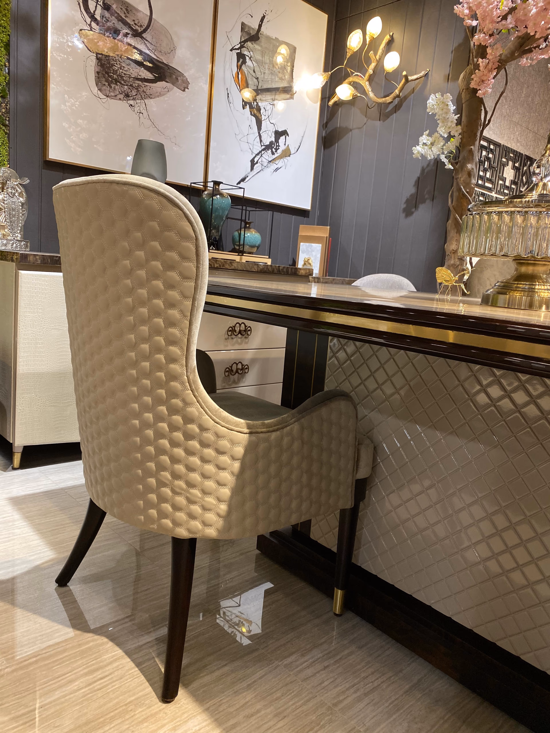 Rear view of a high-back dining chair showing its fully upholstered cream honeycomb-quilted back panel, placed beside a marble-topped console.