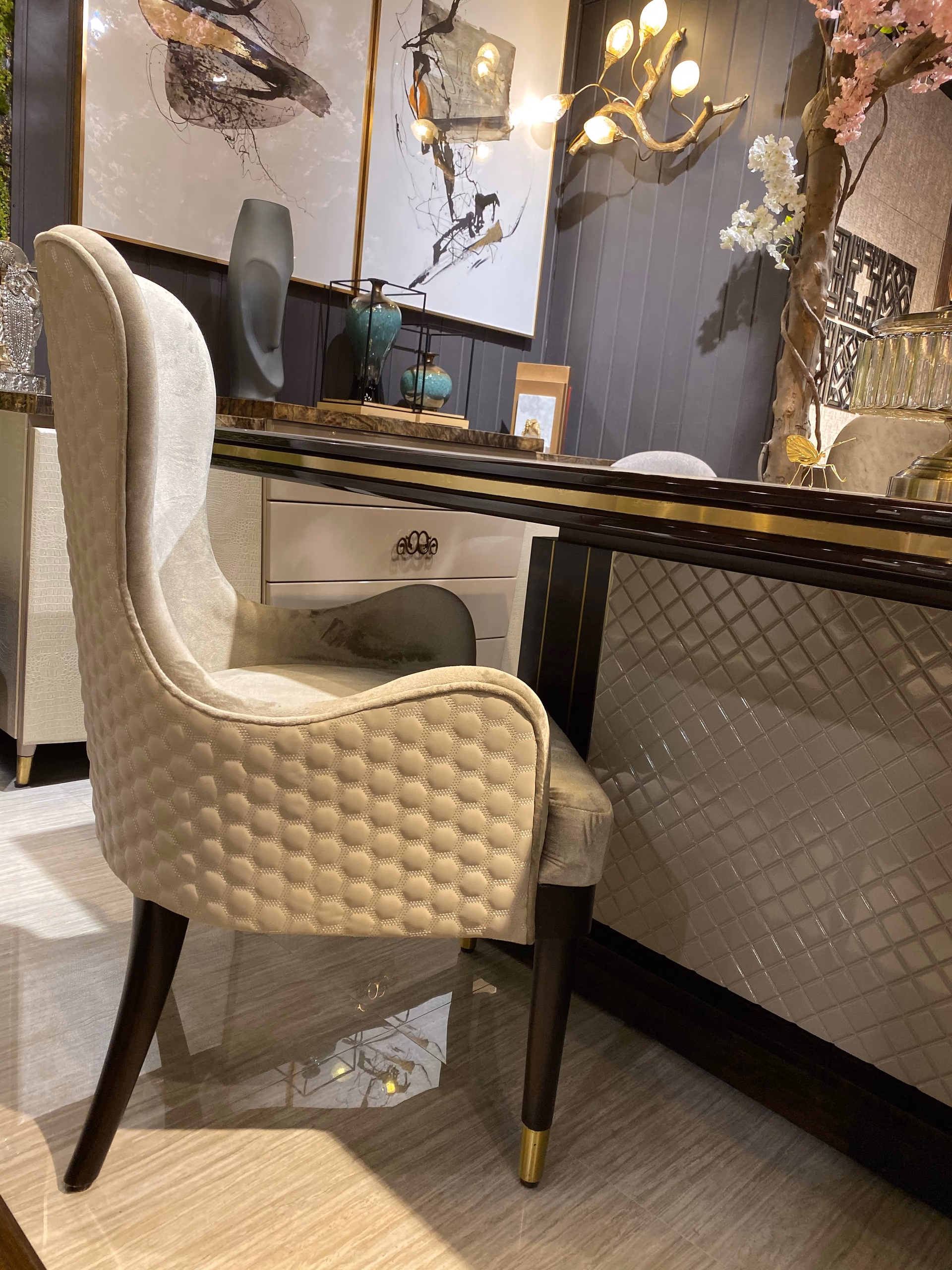 Side profile of a cream honeycomb-quilted wingback dining chair showing its curved arm and gently reclined back on tapered dark wood legs.
