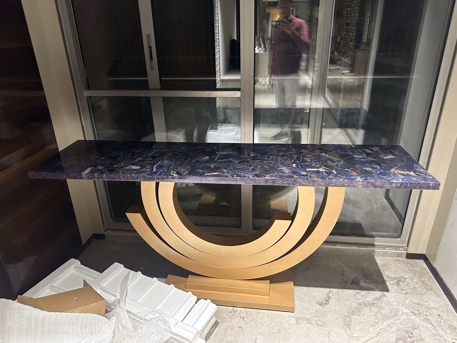 Rectangular console table with a deep blue and gold sodalite stone top resting on a gold ring-shaped base by a window.