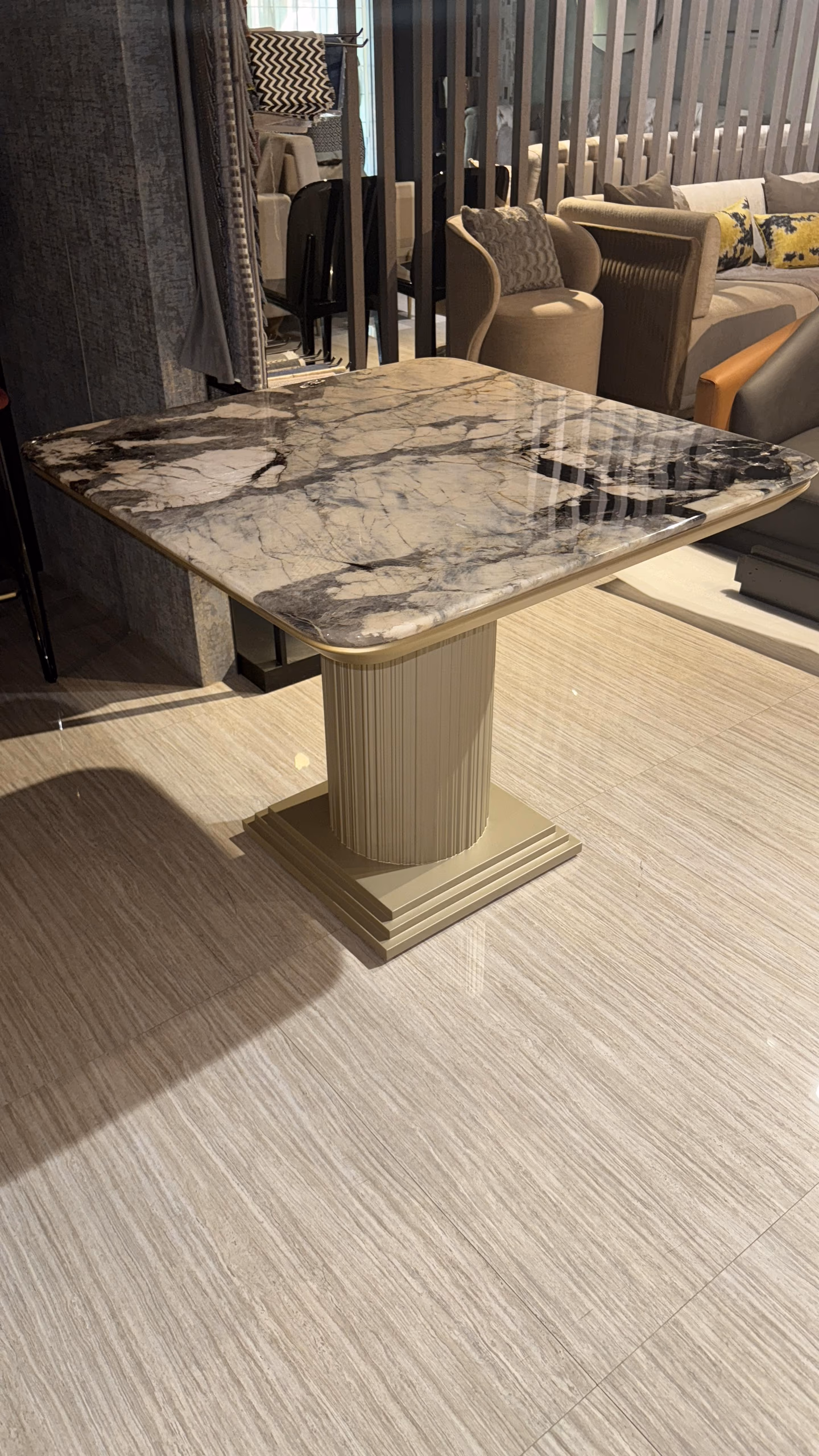 Square dining table with dramatic grey and white veined marble top on a cream fluted round pedestal and stepped base.