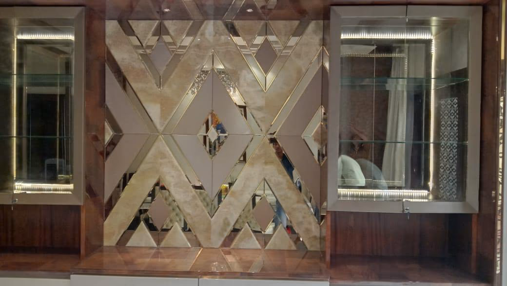 Close view of the display unit's bronze antiqued-mirror centre panel cut in a large diamond and chevron pattern with thin gold lines, between two glass cabinets.