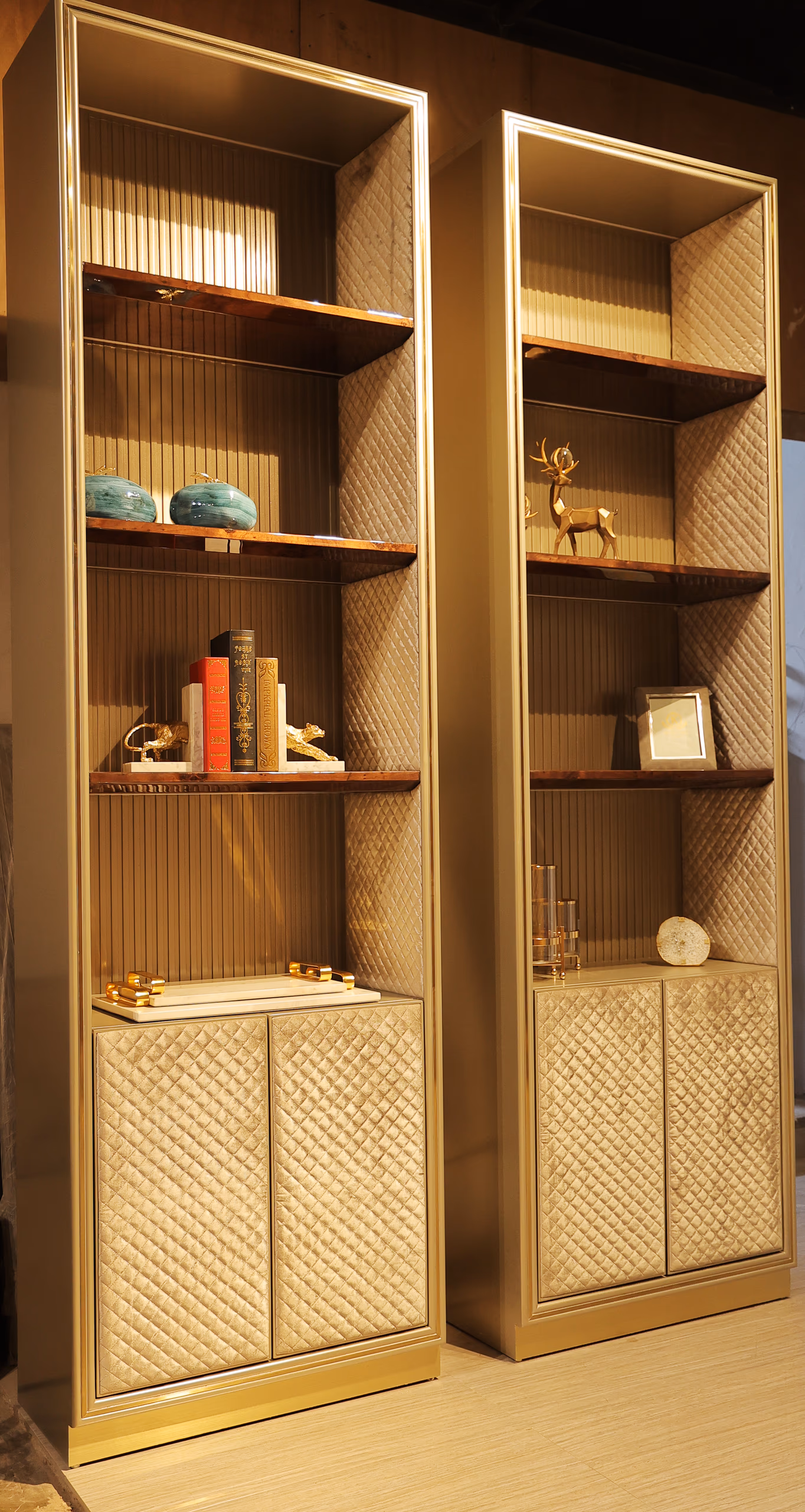 Pair of gold-trim display cabinets with quilted lower doors and open walnut shelving