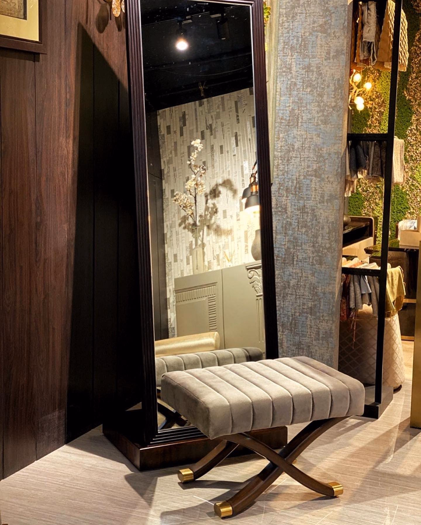 Tall rectangular floor mirror in a deep stepped dark rosewood frame on a moulded plinth base, leaning against panelling beside a channel-tufted X-frame bench.