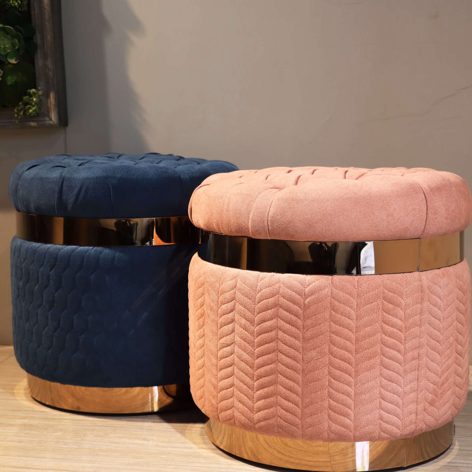Two round tufted vanity stools, one navy blue and one blush pink, with brass banding and wood plinth base.