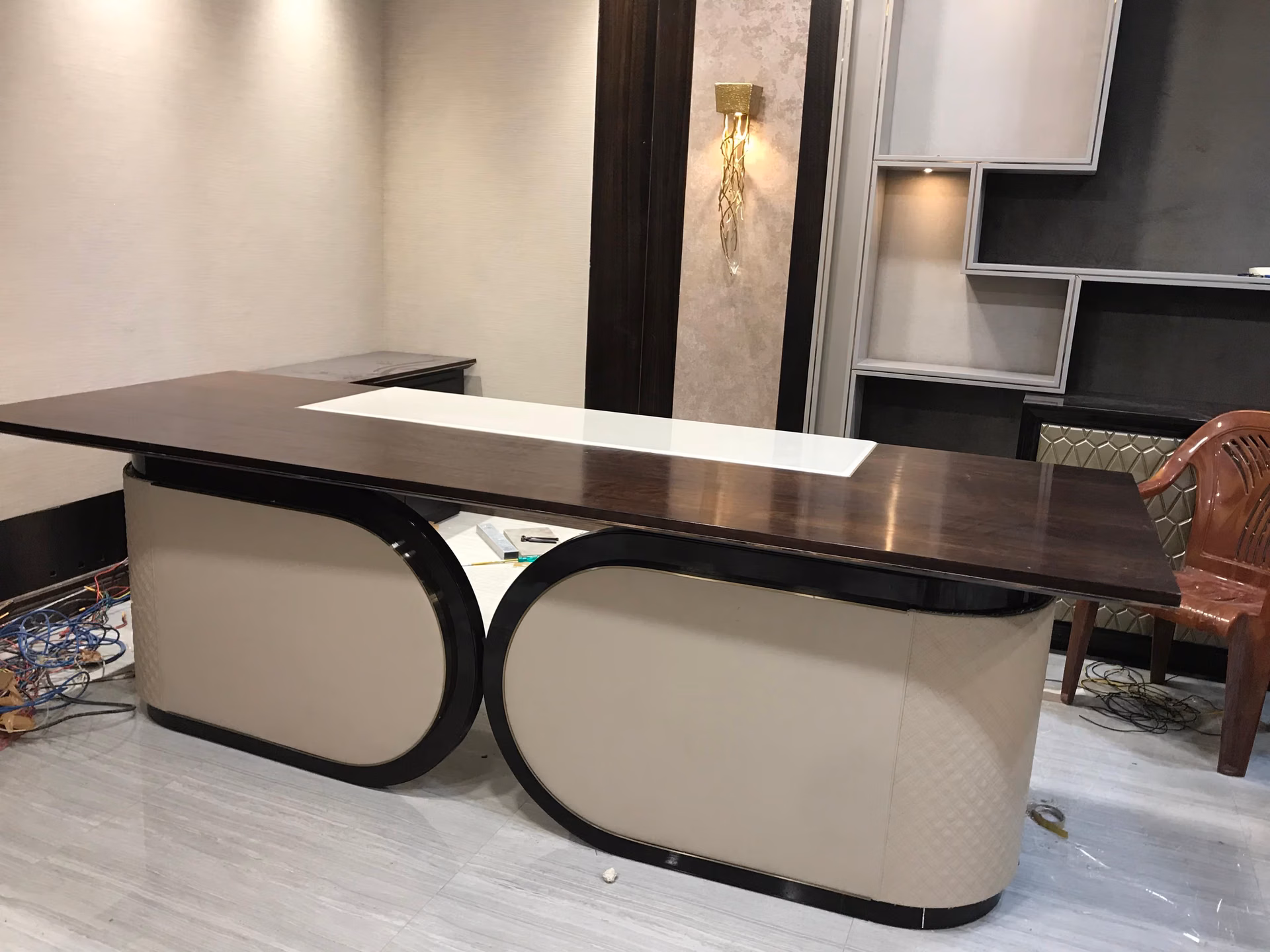 Executive desk with a dark walnut top and white lacquer inset, standing on two oval cream-leather pedestals framed in black gloss, in a room being finished.