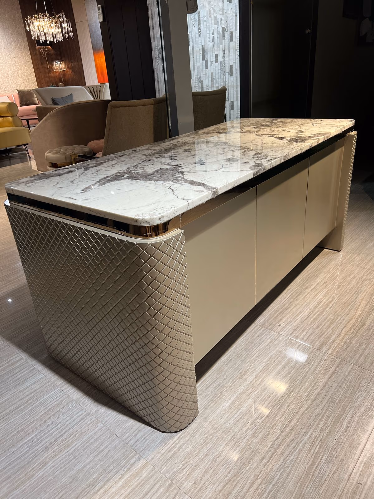 Close-up of a cream lacquer executive desk with a bookmatched grey-veined marble top and quilted leather-textured side panel.