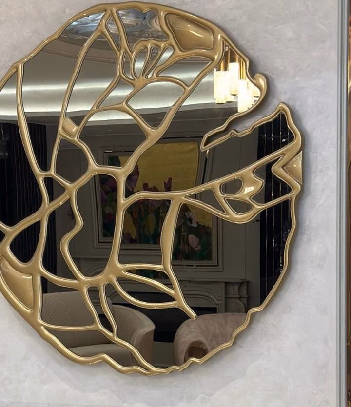 Large round wall mirror with an abstract poured-gold framework running across the glass in organic branching lines, hung on a pale marble-panelled entrance wall.