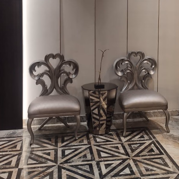 Pair of silver-leafed chairs with open hand-carved scroll and heart-shaped backs, champagne leather seats and cabriole legs, flanking a faceted mirrored side table on an inlaid marble floor.