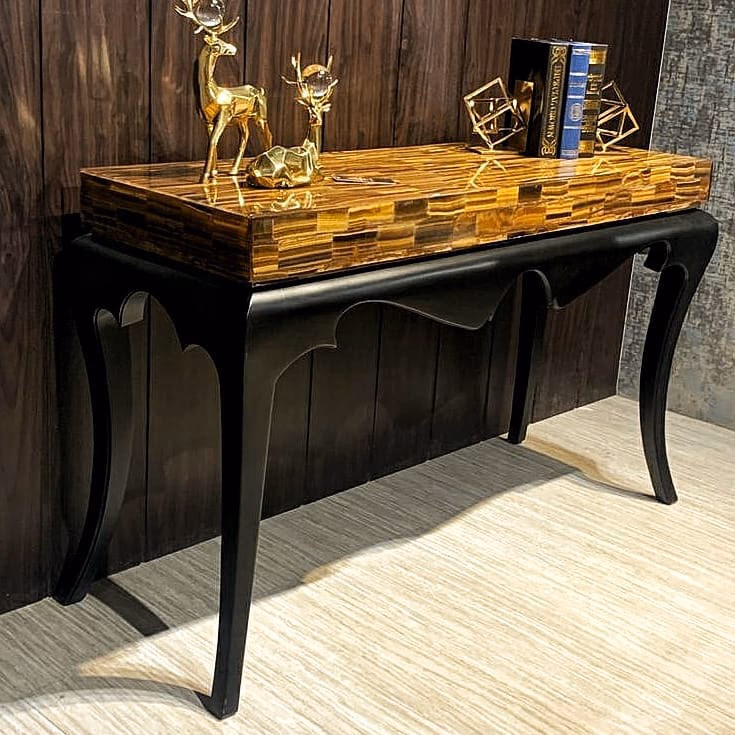 Slim entrance console with a banded golden tiger's eye stone top and a matte black frame on tall curved cabriole legs, styled with brass deer figures and books.